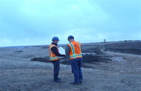 two people in hard hats and reflective vests standing on barren, muddy ground