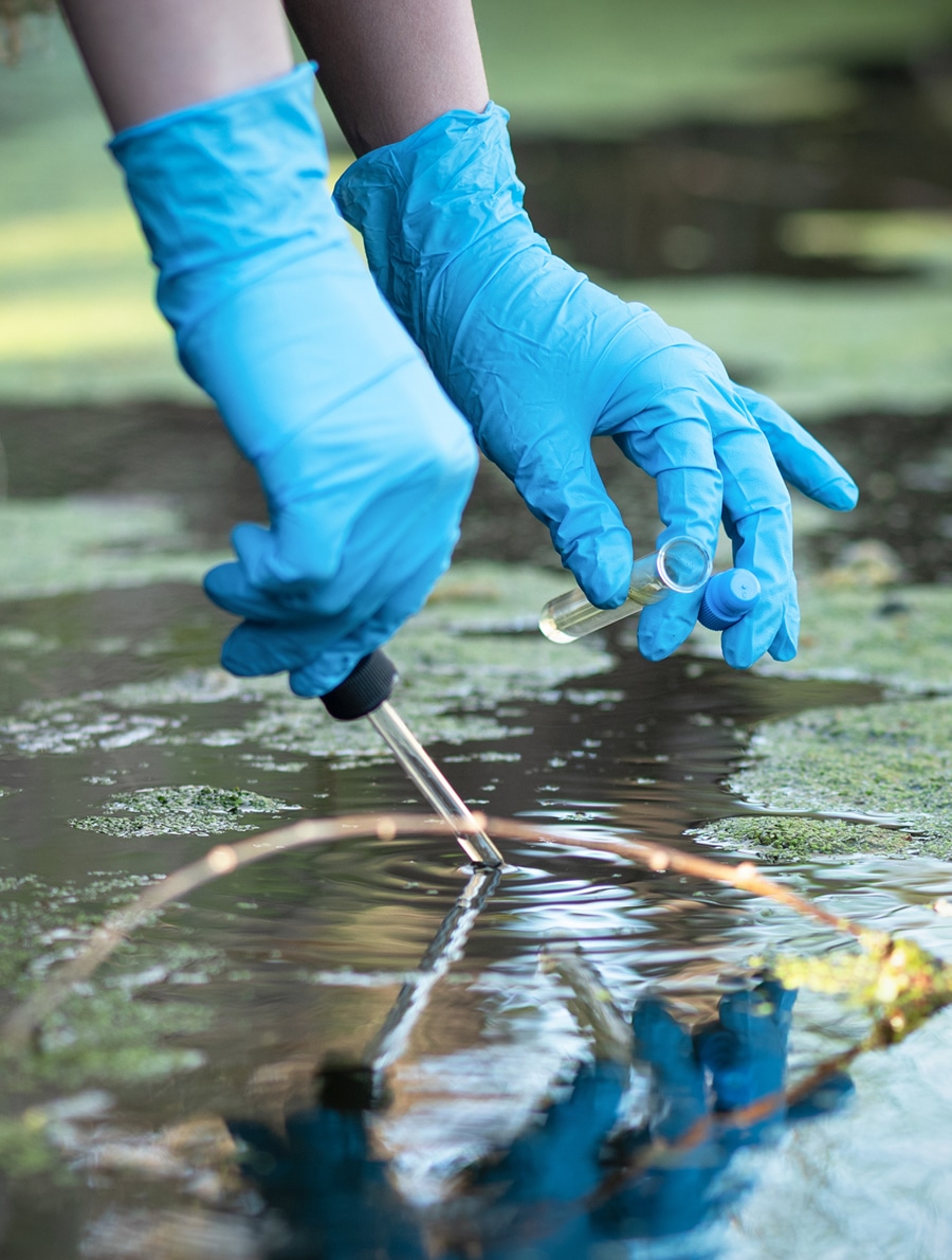Gloved hands collecting stormwater in a test tube for California’s MS4 program
