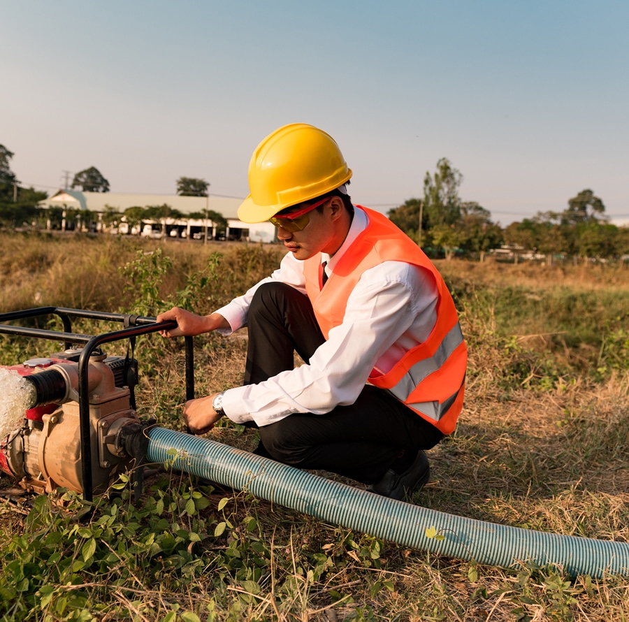 Man in a hard hat and refelctive vest using a water pump in a field as a part of Stormwater Training Center's Stormwater Management Plan Development